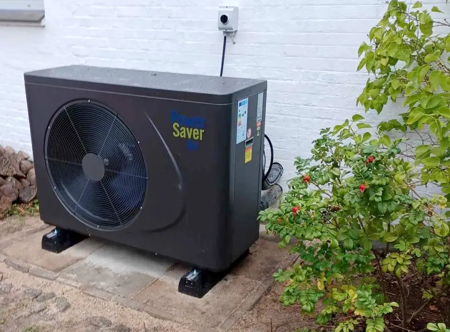 PowerSaverAir luft til vand varmepumpe monteret foran en hvid murstensfacade.